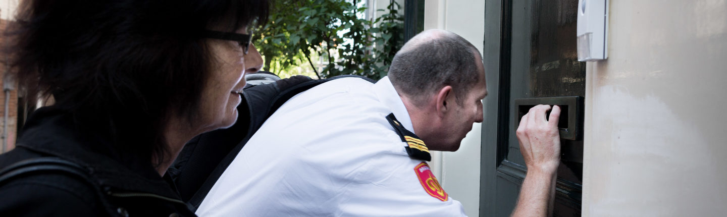 Een handhaver kijkt door een brievenbusgleuf of mensen in het pand aan de Schipperstraat aanwezig zijn.