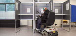 Afbeelding bij Toegankelijkheid van stemlocaties. Een man in een rolstoel brengt zijn stem uit in een stemhokje