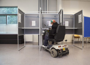 Afbeelding bij Toegankelijkheid van stemlocaties. Een man in een rolstoel brengt zijn stem uit in een stemhokje