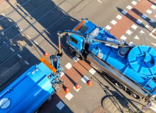 Twee wagens legen het riool op een kruispunt in Amsterdam; een voorbeeld van de uitvoering van de gemeentelijke rioolwatertaken